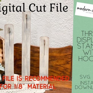 Può includere: Tre espositori in legno bianco con ganci. Ogni espositore ha un gancio nella parte superiore ed è progettato per materiale da 3,2 mm. Gli espositori sono su una superficie in legno con una tovaglia di pizzo bianco. Il testo dell'immagine dice "Digital Cut File", "modern charm HANDCRAFTED", "THREE DISPLAY STANDS WITH HOOKS", "THIS FILE IS RECOMMENDED FOR 1/8" MATERIAL", and "SVG. FILE INSTANT DOWNLOAD".