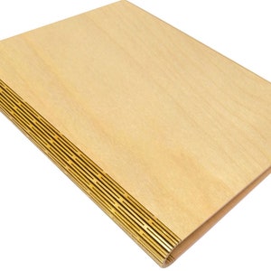May include: A light-colored wooden notebook with a decorative, slotted spine. The cover is made of smooth, light-colored wood. The spine has a series of thin, parallel slots, adding a unique design element to the notebook.