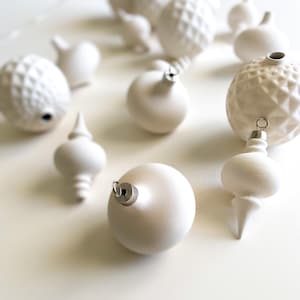 May include: A collection of white Christmas ornaments in various shapes and textures. The ornaments include smooth spheres, textured diamond patterns, and teardrop shapes. Each ornament has a silver metal cap for hanging.