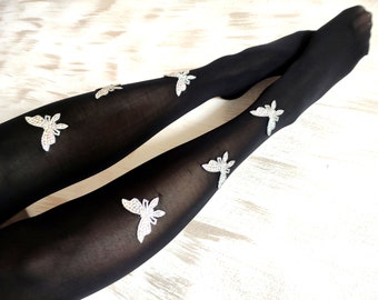 Può includere: Collant neri con un design a farfalla scintillante. Le farfalle sono sparse sui collant, alcune sulle gambe e altre sulle cosce.