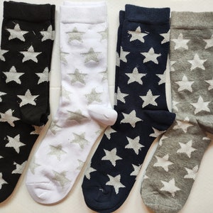 May include: Four pairs of socks with a star pattern. The socks are black, white, navy blue, and gray. The stars are silver.