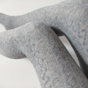 May include: Light grey patterned tights. The tights have a textured knit design with a repeating circular pattern. The fabric looks soft and comfortable, suitable for cooler weather. The tights are shown against a white background.