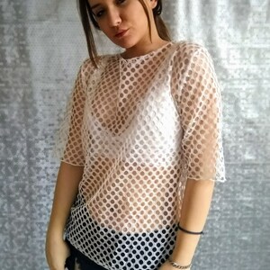 May include: White mesh top with a round pattern. The top is sheer and has short sleeves.