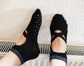 May include: Black ballet-style socks with crisscross straps and a silver glitter trim. The socks have a non-slip grip pattern on the soles. These socks are designed for comfort and style during dance or yoga.