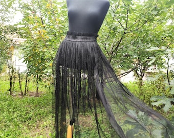 May include: Black sheer skirt with a black fringe trim. The skirt is on a mannequin and is displayed against a green background.