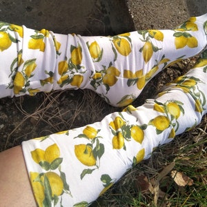 Könnte beinhalten: Ein Paar weiße Kniestrümpfe mit Zitronenmuster. Die Socken sind aus weichem, dehnbarem Stoff und haben ein gelbes Zitronenmuster auf weißem Hintergrund.