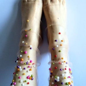 May include: A pair of sheer socks with colorful pearl-like beads scattered across the fabric. The socks are nude-colored and the beads are a variety of colors, including pink, purple, green, yellow, and white.