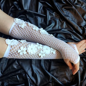 May include: White fishnet gloves with white flower embellishments. The gloves are long and reach past the elbow.