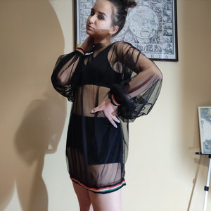 May include: A black sheer dress with long sleeves and a colorful stripe around the hem. The dress is made of a lightweight, breathable fabric and has a relaxed fit.