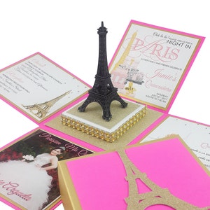 Può includere: Una statuetta nera della Torre Eiffel è posta su una base oro e bianca, circondata da biglietti d'invito rosa e oro. I biglietti presentano testo e illustrazioni, tra cui la Torre Eiffel e i dettagli di un evento Quinceañera.