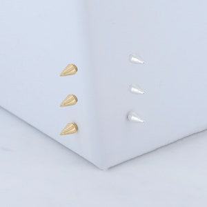 May include: Three gold and three silver cone-shaped studs. The studs are arranged in two vertical rows on a white surface.