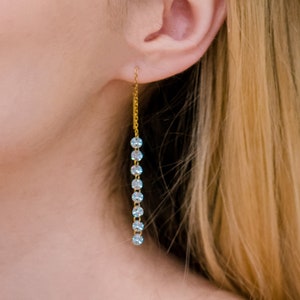 May include: Gold dangle earrings with a chain and clear iridescent stones.