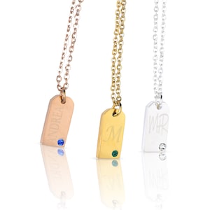 May include: Three gold, silver, and rose gold necklaces with personalized name tags. The tags are engraved with the names "Andrea", "M", and "WHR". Each tag has a small gemstone accent.