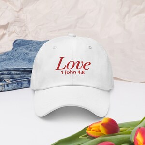Puede incluir: Gorra de béisbol blanca con texto bordado en rojo que dice "Love 1 John 4:8".