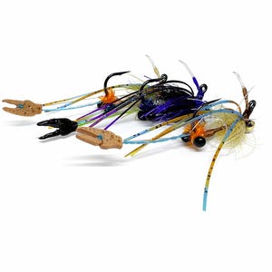 Könnte beinhalten: Nahaufnahme mehrerer farbenfroher Angelköder. Die Köder haben schwarze Haken, Krallen in Beige und verschiedene Farben wie Blau, Orange und Lila. Die Köder sind so konzipiert, dass sie Krabben imitieren und sind vor weißem Hintergrund.