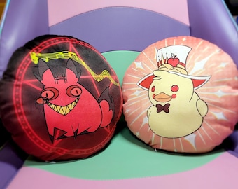 May include: Two round pillows with different cartoon characters. One pillow features a red cartoon fox with a pentagram and musical notes on a black background. The other pillow features a yellow cartoon duck wearing a red and white hat with a red apple on top, on a pink background with white stars.
