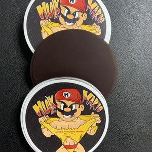 Può includere: Adesivo rotondo con un personaggio dei cartoni animati con berretto rosso e baffi, in posa da supereroe. Il testo "Hulk Mario" è sopra il personaggio e "Eat Your Mushrooms Brother!" è sulla maglietta.