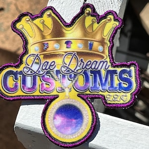 May include: Purple and gold embroidered patch with a crown, a pendant, and the text "Dae Dream Customs".