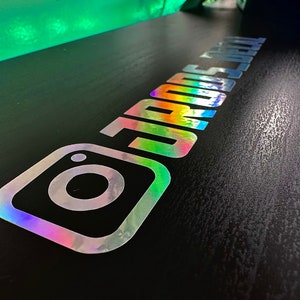May include: A holographic vinyl decal featuring the Instagram logo icon followed by the text "JRODS_DETAIL" in a bold, sans-serif font. The sticker displays a reflective, multi-colored metallic finish that shifts in appearance under light.