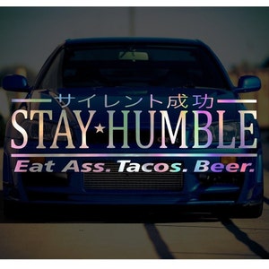 May include: A blue car with a sticker that says "Stay Humble" and "Eat Ass. Tacos. Beer." in a rainbow font.