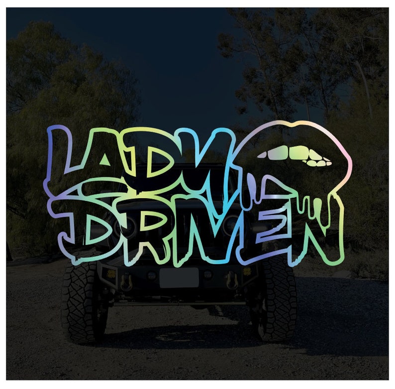 Pu&ograve; includere: Una Jeep nera con un adesivo colorato "Lady Driven" sul lunotto posteriore. L'adesivo presenta un design di rossetto che cola.
