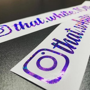 May include: Two rectangular white vinyl stickers featuring the Instagram logo and the text that.white.10thgen in a purple holographic finish. The holographic material displays a reflective, multi-colored glitter effect across the surface.