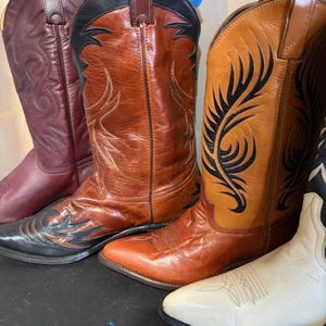 May include: A collection of cowboy boots in various colors. The boots include shades of burgundy, brown, and white. The boots have decorative stitching and pointed toes. The boots are made of leather and have a classic Western design.