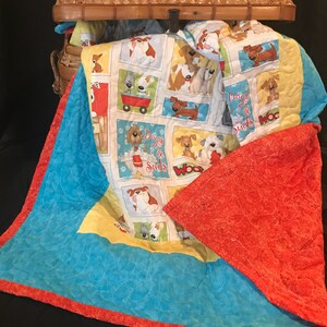 K&ouml;nnte beinhalten: Eine blaue und orangefarbene gesteppte Decke mit einem gelben und wei&szlig;en Stoffpanel mit Cartoon-Hunden und dem Text "Dogs Go & Suds".