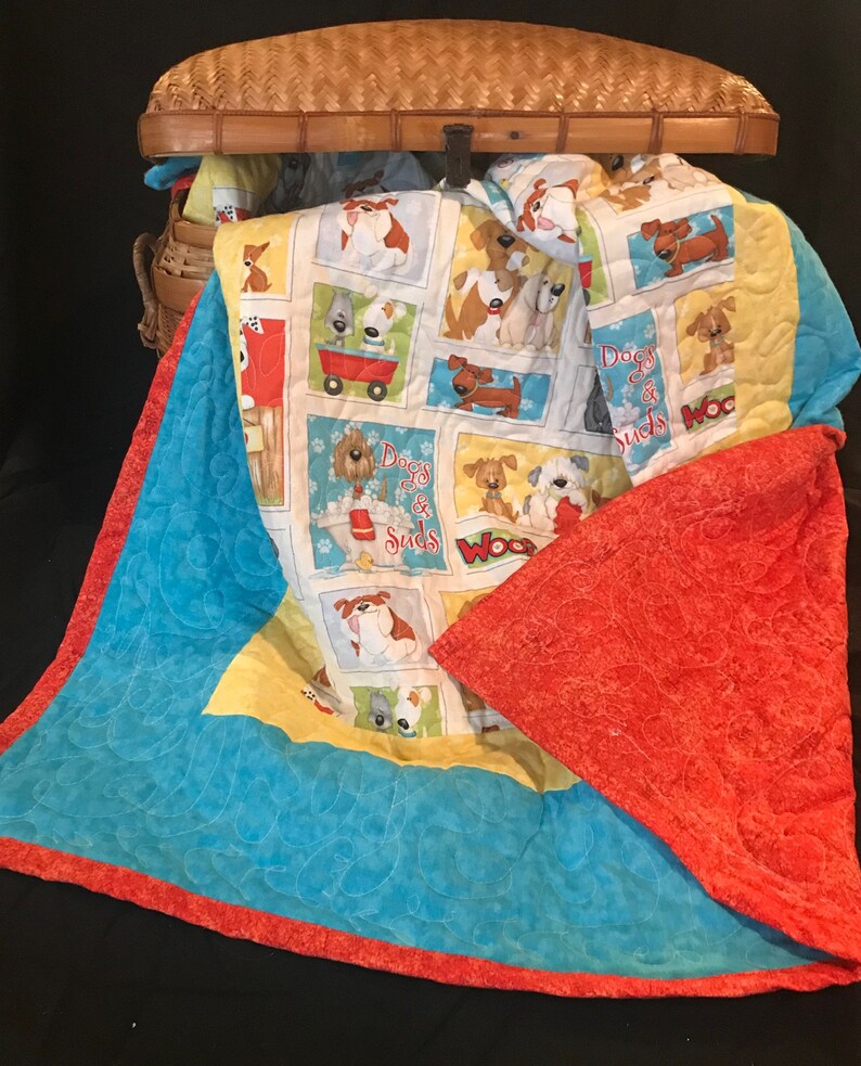 K&ouml;nnte beinhalten: Eine blaue und orangefarbene gesteppte Decke mit einem gelben und wei&szlig;en Stoffpanel mit Cartoon-Hunden und dem Text "Dogs Go & Suds".
