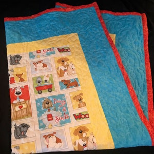 K&ouml;nnte beinhalten: Eine gelbe und blaue gesteppte Decke mit rotem Rand. Die Decke zeigt ein sich wiederholendes Muster von Hunden und den Text "Dogs & Suds" und "Woo".