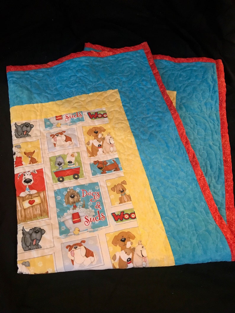 K&ouml;nnte beinhalten: Eine gelbe und blaue gesteppte Decke mit rotem Rand. Die Decke zeigt ein sich wiederholendes Muster von Hunden und den Text "Dogs & Suds" und "Woo".