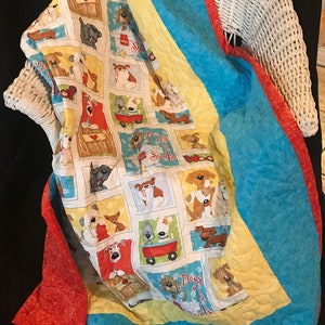 K&ouml;nnte beinhalten: Eine farbenfrohe Decke mit Hundemotiven. Die Decke zeigt verschiedene Hunderassen in verschiedenen Posen, darunter eine Bulldogge, ein Dackel und ein Pudel. Die Decke ist mit einem wei&szlig;en Hintergrund gefertigt und hat einen roten, gelben und blauen Rand.