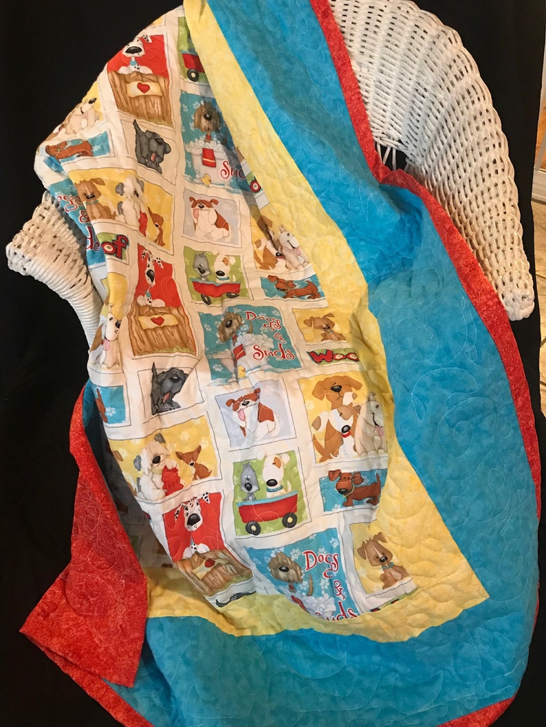 K&ouml;nnte beinhalten: Eine farbenfrohe Decke mit Hundemotiven. Die Decke zeigt verschiedene Hunderassen in verschiedenen Posen, darunter eine Bulldogge, ein Dackel und ein Pudel. Die Decke ist mit einem wei&szlig;en Hintergrund gefertigt und hat einen roten, gelben und blauen Rand.