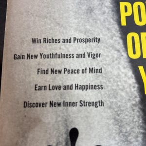 May include: Close-up of a book page with text in black font. The text includes phrases like "Win Riches and Prosperity" and "Gain New Youthfulness and Vigor." The word "POWER" is visible in yellow.