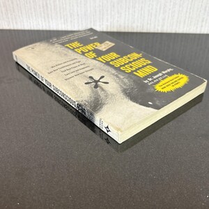 May include: A paperback book titled "The Power of Your Subconscious Mind" by Dr. Joseph Murphy. The cover features a black and white image of a face and the title in yellow and white. The book is on a dark surface.