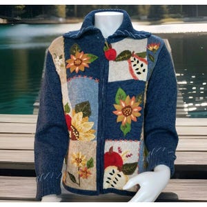 Könnte beinhalten: Ein blauer Strickcardigan mit Reißverschluss und gestickten Blumen- und Fruchtmotiven. Der Cardigan hat ein Patchwork-Design mit verschiedenen farbigen Quadraten.