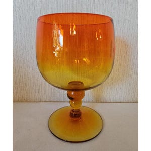 May include: A large, amber-colored glass goblet with a wide bowl and a short stem. The bowl is a gradient of orange and yellow, with a clear base.