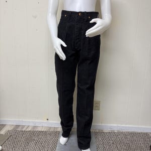 May include: High-waisted black denim jeans featuring a button fly closure, front pleats, and copper-toned rivets at the pockets. These straight-leg trousers are constructed from a dark, solid-coloured fabric with visible vertical stitching details.