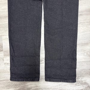 May include: A pair of dark charcoal grey trousers featuring a straight-leg cut and a visible vertical crease running down the centre of each leg. The fabric has a textured, woven appearance with a consistent dark grey tone throughout the garment.