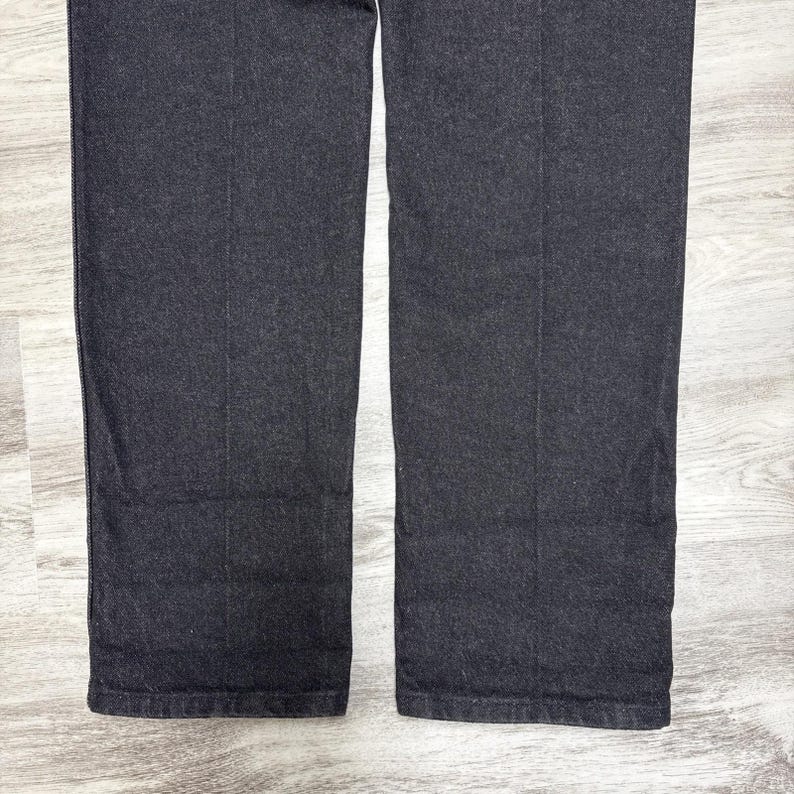 May include: A pair of dark charcoal grey trousers featuring a straight-leg cut and a visible vertical crease running down the centre of each leg. The fabric has a textured, woven appearance with a consistent dark grey tone throughout the garment.