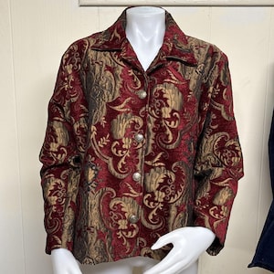 May include: A burgundy and gold brocade jacket with a button-up front and a notched collar. The jacket features a detailed floral pattern and silver-toned buttons. The sleeves are long, and the jacket is displayed on a mannequin.