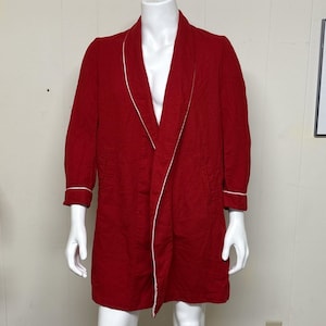 May include: A solid red robe featuring a shawl collar and long sleeves with white piping trim along the edges of the collar, front opening, and sleeve cuffs. The garment has a straight hemline and two side pockets, displayed on a white mannequin.