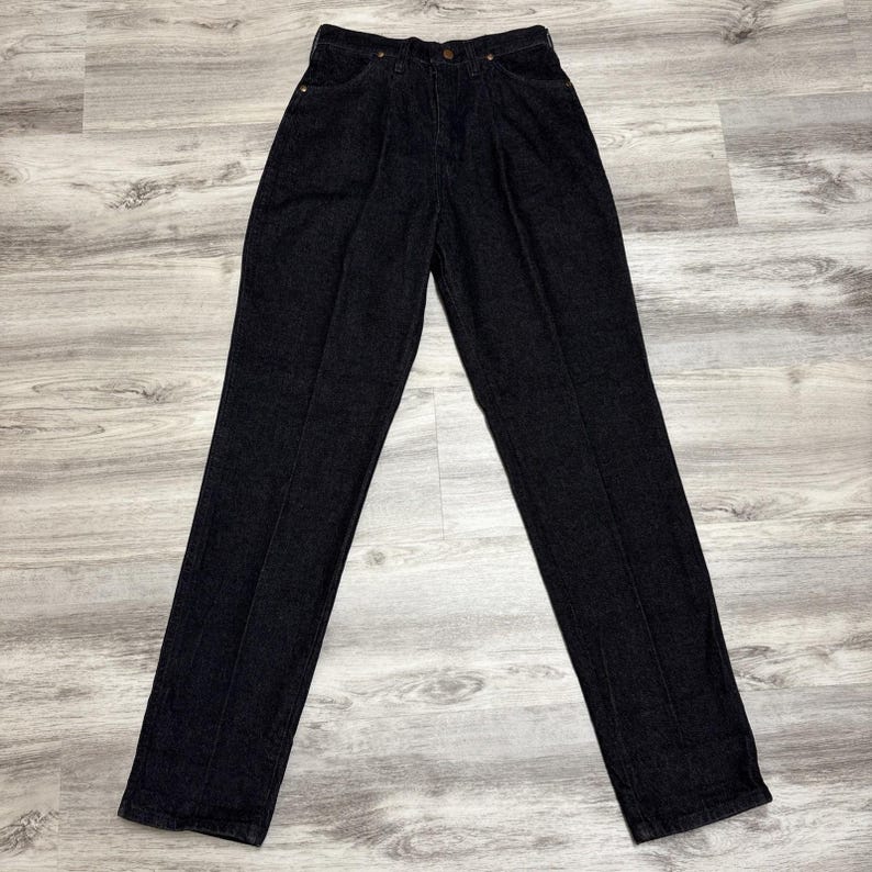 May include: A pair of high-waisted black denim jeans featuring a straight-leg cut, a button and zip fly closure, and visible vertical seams running down the front of each leg. The fabric has a solid dark black wash with tonal stitching.