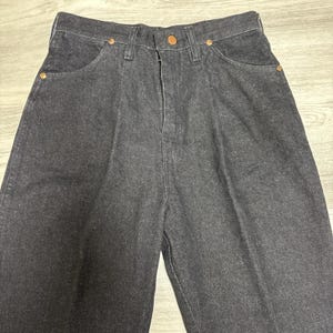 May include: High-waisted dark charcoal denim jeans featuring a front button closure, a zip fly, and copper-toned metal rivets at the pocket corners. The trousers have a structured waistband with belt loops and a classic five-pocket design.