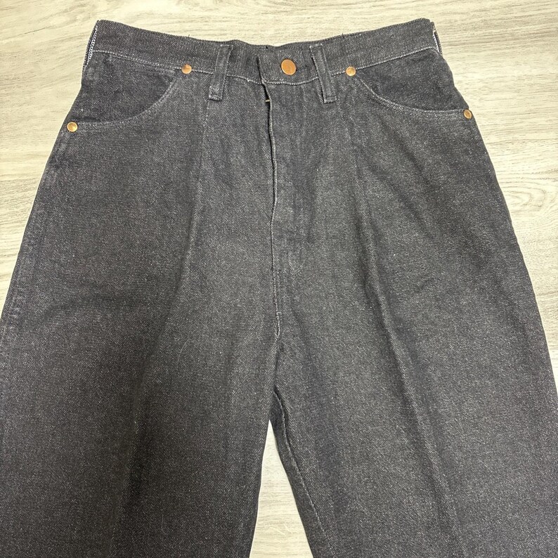 May include: High-waisted dark charcoal denim jeans featuring a front button closure, a zip fly, and copper-toned metal rivets at the pocket corners. The trousers have a structured waistband with belt loops and a classic five-pocket design.