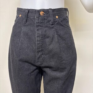May include: High-waisted black denim jeans featuring a structured waistband with a single copper-toned button closure, belt loops, and two front pockets reinforced with small copper-toned rivets. The fabric has a visible twill weave texture.