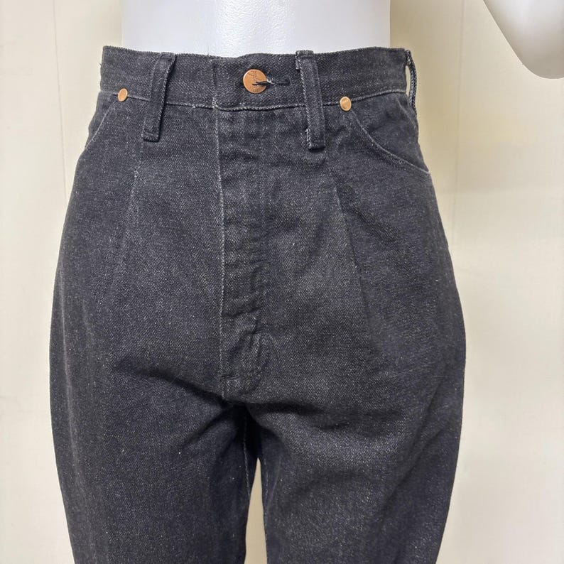 May include: High-waisted black denim jeans featuring a structured waistband with a single copper-toned button closure, belt loops, and two front pockets reinforced with small copper-toned rivets. The fabric has a visible twill weave texture.