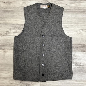 May include: A gray wool vest with a V-neck and a button-up front. The vest has two front pockets and a small label near the collar. The vest is made of a thick, textured fabric.