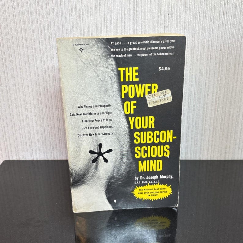 May include: A vintage paperback book titled "The Power of Your Subconscious Mind" by Dr. Joseph Murphy. The cover is black and white with the title in large yellow letters. The book promises to help readers win riches, gain youthfulness, and find inner strength.