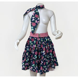 May include: A navy blue skirt and scarf set with a pink belt. The skirt and scarf feature a floral and butterfly pattern with pink roses and butterflies. The belt is pink with a silver buckle.